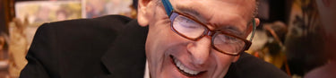 Marc Kravit wearing glasses and a suit, smiling broadly with a blurred background
